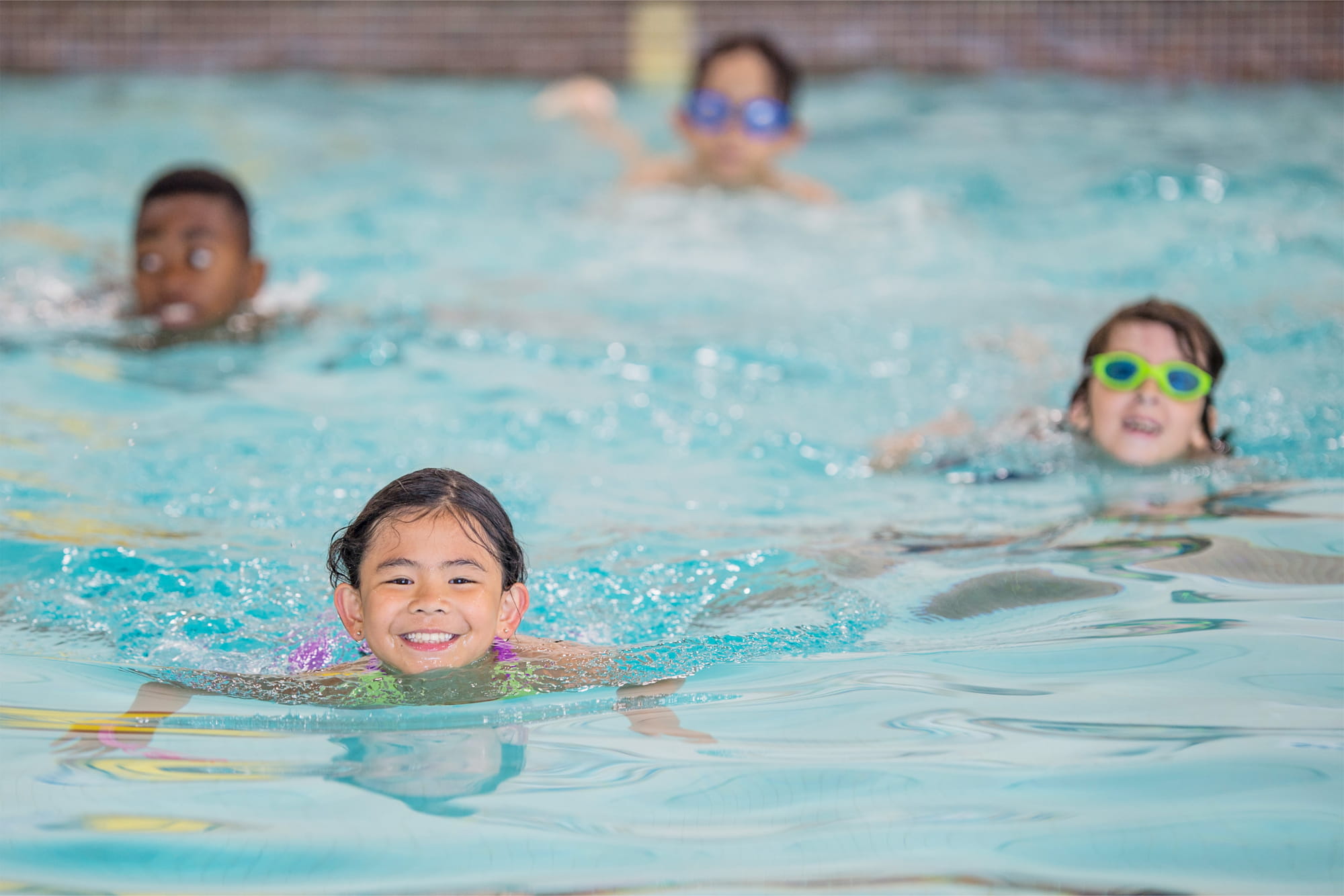 Four children swimming in pool smiling